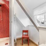 Shower area with red tiles and red chair under sloped roof.