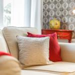 A sofa with cushions near a window and a red sideboard.