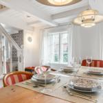 Dining table for four, red chairs, windows with white curtains.