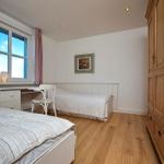 Zimmer mit zwei Betten, Schreibtisch und Holzschrank. Fenster mit Vorhängen und Wandbild.