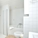 Badezimmer mit Dusche, Badewanne und Toilette. Weiße Fliesen und Handtücher.