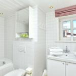 Badezimmer mit Badewanne, Waschbecken und Toilette. Weiße Fliesen und Fenster mit Rollladen.