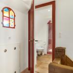 Hallway with colorful window, door to bathroom with toilet and shower.