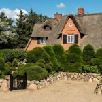 Traditionelles Haus mit Strohdach, umgeben von grünen Hecken und Steinmauern.