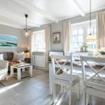 Living and dining area with white table, chairs, and sofa. Stone floor and large windows.