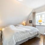 Bedroom with sloped ceiling, bed, nightstand, TV, and window.