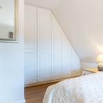 Bedroom with white wardrobe, mirror, and bedside table with lamp.
