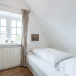 A bedroom with sloped ceiling, white bed, and window with curtains.