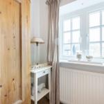 A room with wooden wardrobe, white cabinet, and window with curtains.