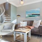 Living room with sofa, armchair, table, and wall art. Staircase in the background.