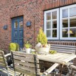 Wooden table and chairs in front of red brick house with blue door and white windows.