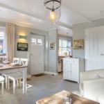 Dining area with table, chairs, and windows. Living area with sofa and kitchenette.