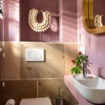Bad mit rosa Wänden, Waschbecken und Toilette. Goldrand-Spiegel und Dekoration.