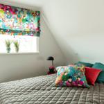 Schlafzimmer mit Bett, Fenster und bunten Vorhängen und Kissen.
