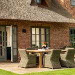 Haus mit Strohdach, Terrasse mit Tisch und Stühlen, Holztisch, Wickerstühle, Steinmauer, Fenster und Tür.