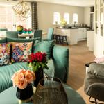 Wohnzimmer mit grünem Sofa, Blumen und Blick in die Küche.