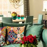 Ein Wohnzimmer mit grünem Sofa, bunten Kissen und Blumenarrangements.