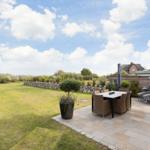 Terrasse mit Sitzgruppe und Blick auf Grünfläche und Himmel.