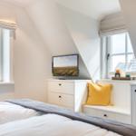 Schlafzimmer mit Dachschrägen, Fenstern, Bett und Fernseher.