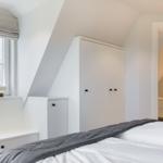 Schlafzimmer mit Dachschrägen, weißem Schrank und Fenster mit Blick auf Dächer.