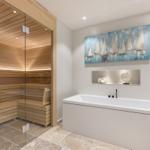 Dusche mit Holzsauna und Badewanne mit Wandbild.
