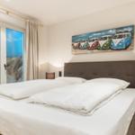 Schlafzimmer mit Bett, Fenster und Wandbild von VW-Bussen.