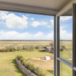 Blick aus dem Fenster auf Grasland und Himmel mit Wolken.