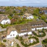 House with thatched roof and garden, view of coastal landscape.