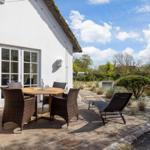 Terrace with table, chairs, and lounge chair. View into garden with trees and shrubs.