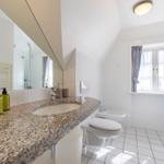Bathroom with sink, toilet, and shower. Window with curtains.