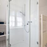 Shower enclosure with glass door, showerhead, and heater on the wall.