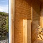 Wooden sauna with entrance door and outdoor view of garden.
