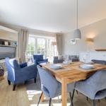 Dining area with wooden table, blue chairs, and window view. Living area with TV and seating.