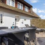 Terrace with table, chairs, and loungers in front of a house with thatched roof.