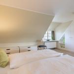 Bedroom with sloped ceiling, bed, wardrobe, and window.