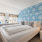 Bedroom with blue-and-white patterned wall, white bed, and windows with outdoor view.