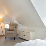 Bedroom with sloped ceiling, armchair, dresser, and window.
