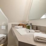 Bathroom with sink, mirror and toilet under sloped ceiling