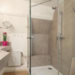 Bath with shower, sink, and mirror. A pink pot with tulips sits on the countertop.