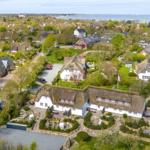 House with thatched roof, garden, and view of the water