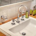 Sink with chrome faucet and green bottles on marble countertop.