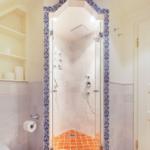 Bathroom with shower, toilet, and shelf. Shower area with glass door and blue patterned frame.