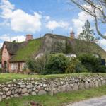 Traditional house with green roof, stone wall, and trees in the front garden.
