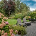 Garten mit Sitzgelegenheiten und Blumenbeeten auf gepflastertem Platz.