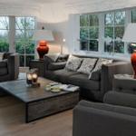 Wohnzimmer mit grauen Sofas, Holzboden und großen Fenstern.