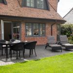 Terrasse mit Sitzgruppe und Garten. Haus mit Ziegeldach und Backsteinfassade.