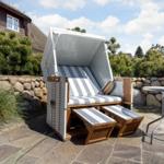 Hocker mit Streifen, Tisch und Steinterrasse vor einem Haus