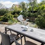 Terrasse mit Tisch und Stühlen, umgeben von Grünflächen und Steinmauern.