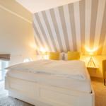 Schlafzimmer mit Bett, gelben Kissen und gestreifter Wand