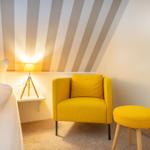 Schlafzimmer mit gelber Sitzgelegenheit und gestreifter Decke.